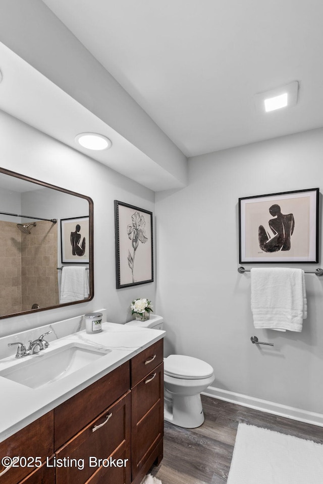 bathroom with wood finished floors, toilet, vanity, a shower, and baseboards