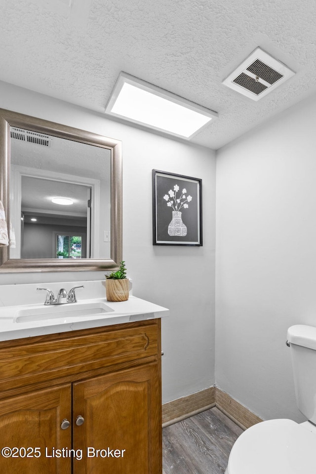 bathroom with wood finished floors, a textured ceiling, toilet, vanity, and baseboards