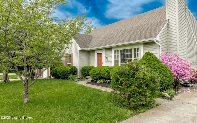 view of front of home with roof with shingles, a front yard, and a chimney