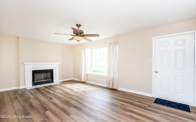 unfurnished living room with a ceiling fan, wood finished floors, baseboards, and a fireplace with flush hearth