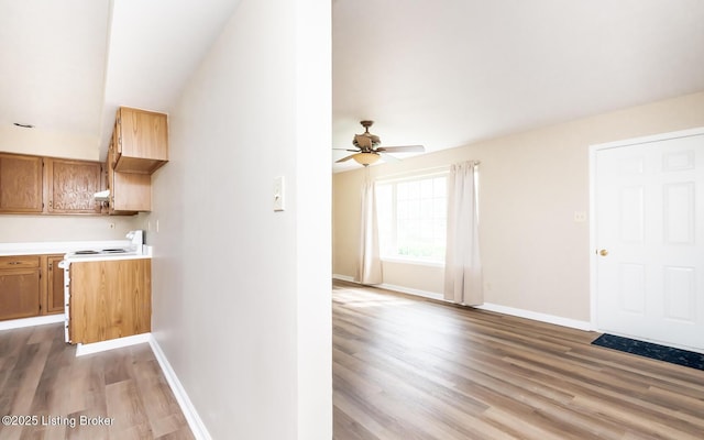 kitchen with electric stove, light wood-style flooring, light countertops, a ceiling fan, and baseboards