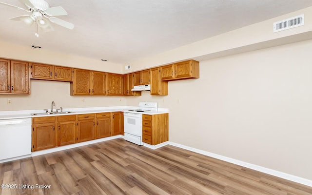 kitchen featuring a sink, white appliances, under cabinet range hood, light wood-style flooring, and brown cabinets