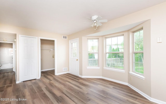 unfurnished bedroom featuring wood finished floors, baseboards, a closet, a spacious closet, and ceiling fan