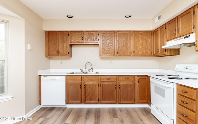 kitchen featuring white appliances, under cabinet range hood, a sink, light wood-style floors, and light countertops