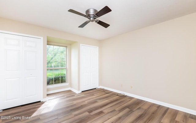 unfurnished bedroom featuring baseboards, wood finished floors, multiple closets, and ceiling fan