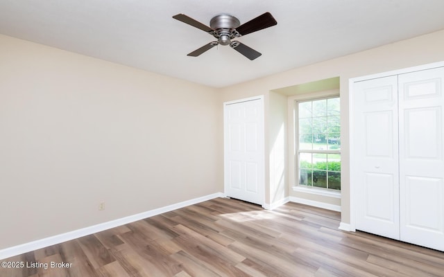 unfurnished bedroom featuring wood finished floors, baseboards, multiple closets, and ceiling fan