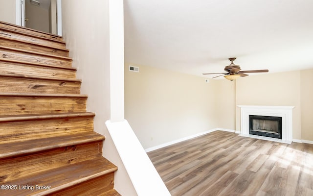 stairway featuring ceiling fan, wood finished floors, baseboards, and a fireplace with flush hearth