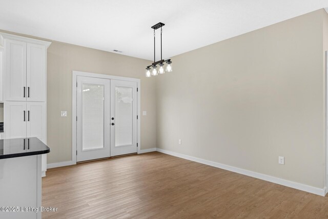 unfurnished dining area with light wood-type flooring, french doors, and baseboards