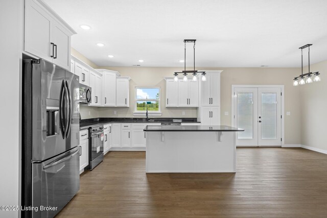 kitchen with stainless steel appliances, dark countertops, white cabinetry, dark wood-style floors, and a center island