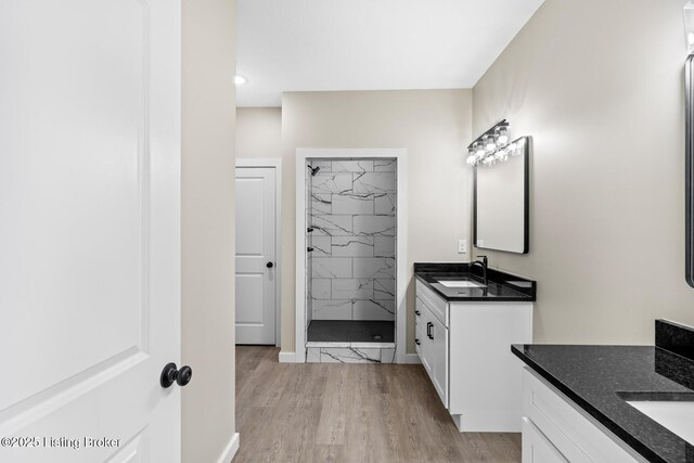 full bath featuring a shower stall, two vanities, wood finished floors, baseboards, and recessed lighting