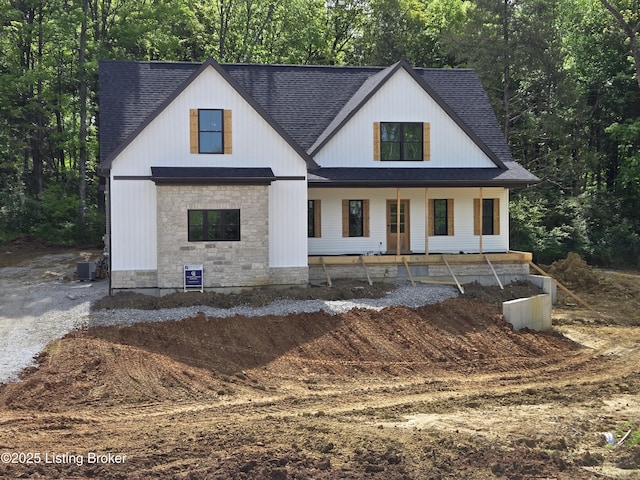 modern farmhouse style home featuring roof with shingles, a porch, stone siding, and cooling unit
