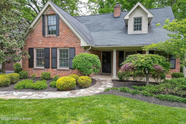 view of front of home with brick siding, a chimney, a shingled roof, and a front lawn