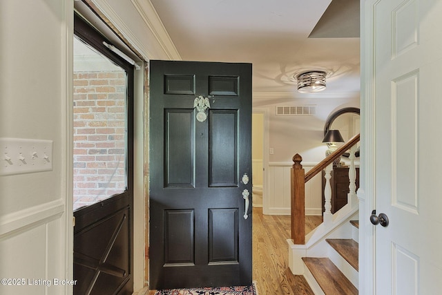 entrance foyer with a decorative wall, crown molding, wainscoting, wood finished floors, and stairway