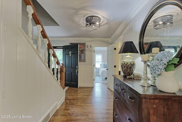 foyer with wood finished floors, stairway, a decorative wall, wainscoting, and crown molding