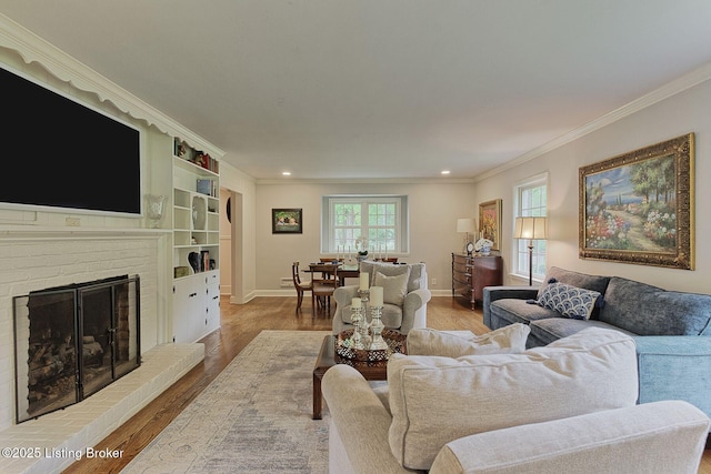 living area with crown molding, wood finished floors, baseboards, a brick fireplace, and recessed lighting
