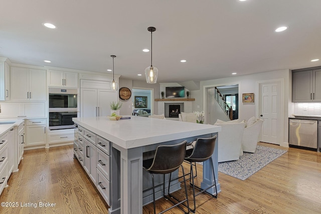 kitchen featuring appliances with stainless steel finishes, open floor plan, recessed lighting, light wood-type flooring, and light countertops