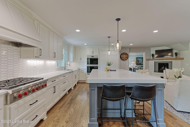 kitchen with appliances with stainless steel finishes, premium range hood, a kitchen bar, white cabinets, and a sink