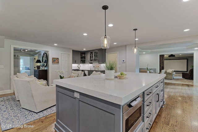 kitchen featuring gray cabinetry, light wood-style floors, a center island, stainless steel microwave, and open floor plan