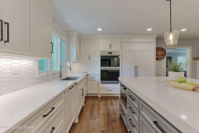 kitchen featuring stainless steel appliances, a sink, light stone counters, backsplash, and dark wood-type flooring