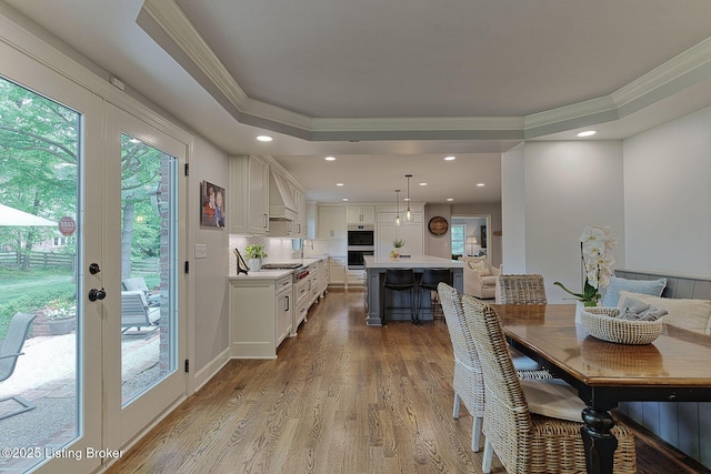 dining space featuring crown molding, wood finished floors, recessed lighting, a raised ceiling, and french doors