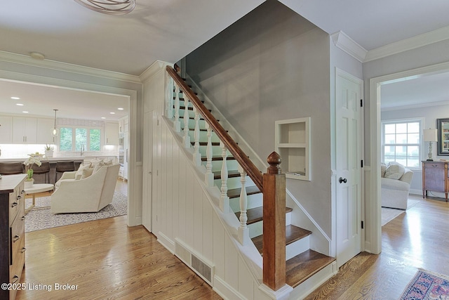 stairway featuring wood finished floors, healthy amount of natural light, crown molding, and built in features
