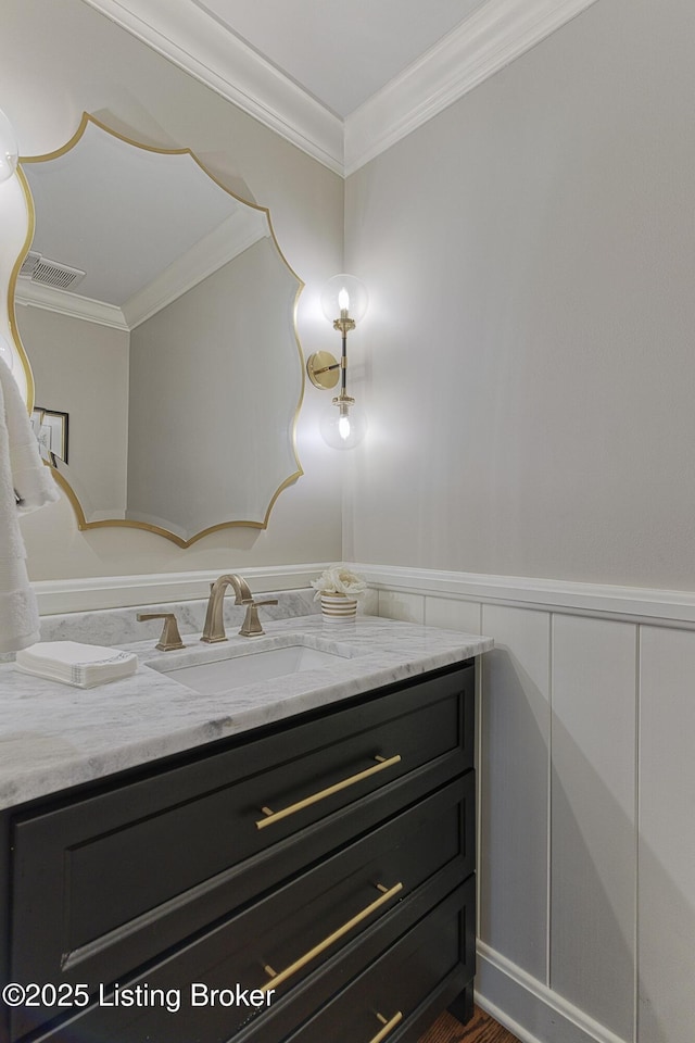 bathroom with crown molding, vanity, a wainscoted wall, and a decorative wall