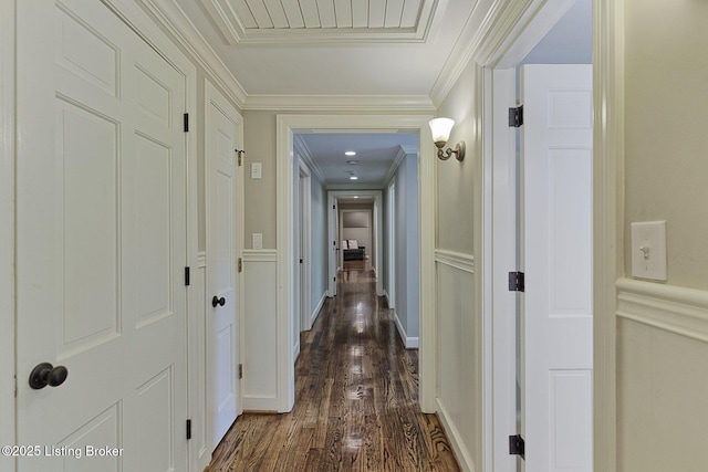 hall with dark wood-style floors, a decorative wall, crown molding, and a wainscoted wall