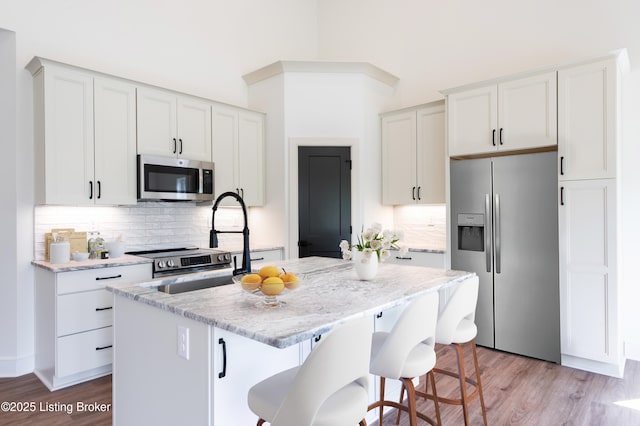 4227 Stilger Cir, Louisville, KY 40299 - kitchen featuring appliances with stainless steel finishes, a kitchen island with sink, light wood-style flooring, and decorative backsplash