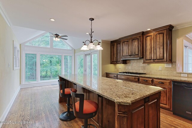 kitchen featuring black dishwasher, a ceiling fan, a kitchen island, light stone countertops, and light wood-type flooring