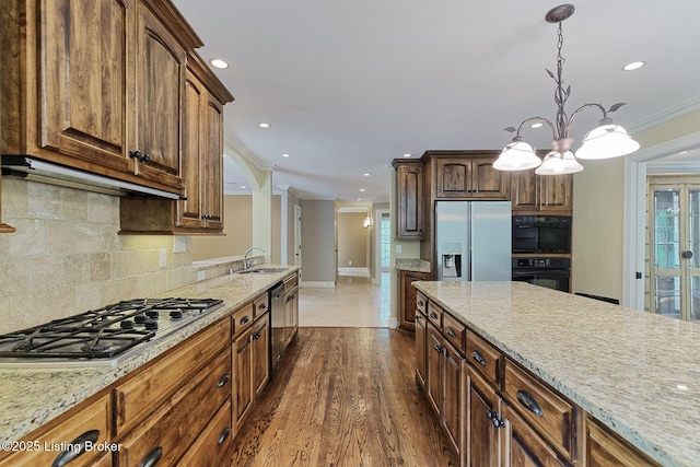 kitchen with stainless steel appliances, crown molding, a sink, under cabinet range hood, and light stone counters