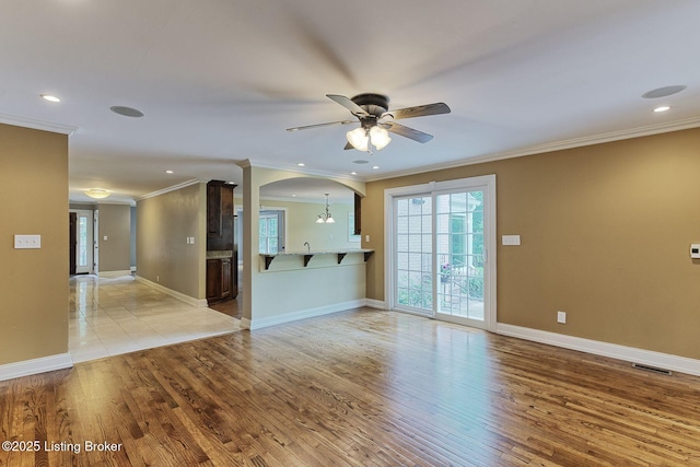 unfurnished living room with ornamental molding, ceiling fan, arched walkways, light wood finished floors, and baseboards