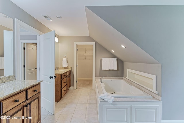 full bath featuring tile patterned flooring, a bath, vaulted ceiling, a walk in closet, and vanity