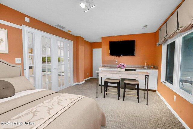 bedroom with light carpet, french doors, baseboards, and a sink