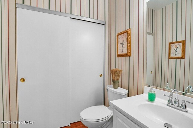bathroom featuring toilet, vanity, and wallpapered walls