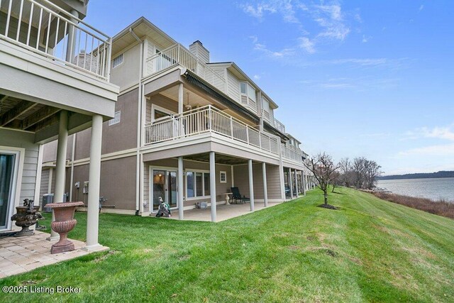 back of property featuring a water view, a patio, a lawn, and a chimney