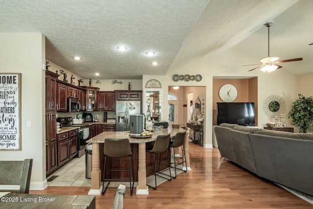 kitchen with stainless steel appliances, open floor plan, a breakfast bar area, dark brown cabinets, and a ceiling fan
