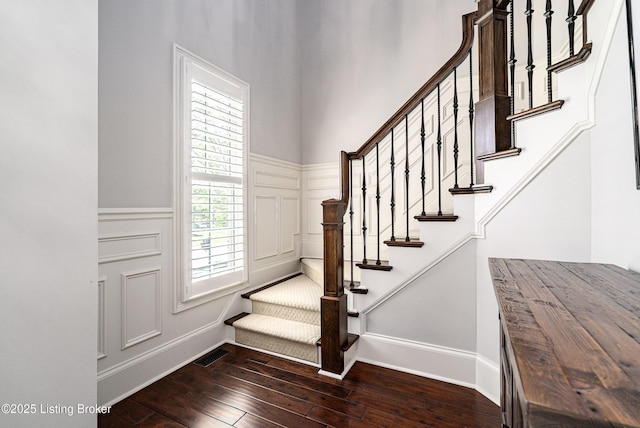 staircase with hardwood / wood-style floors, a wainscoted wall, a decorative wall, and baseboards