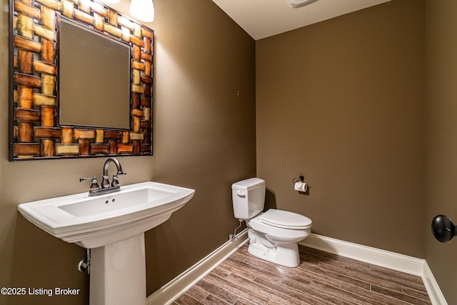 half bathroom featuring baseboards, toilet, and wood finished floors