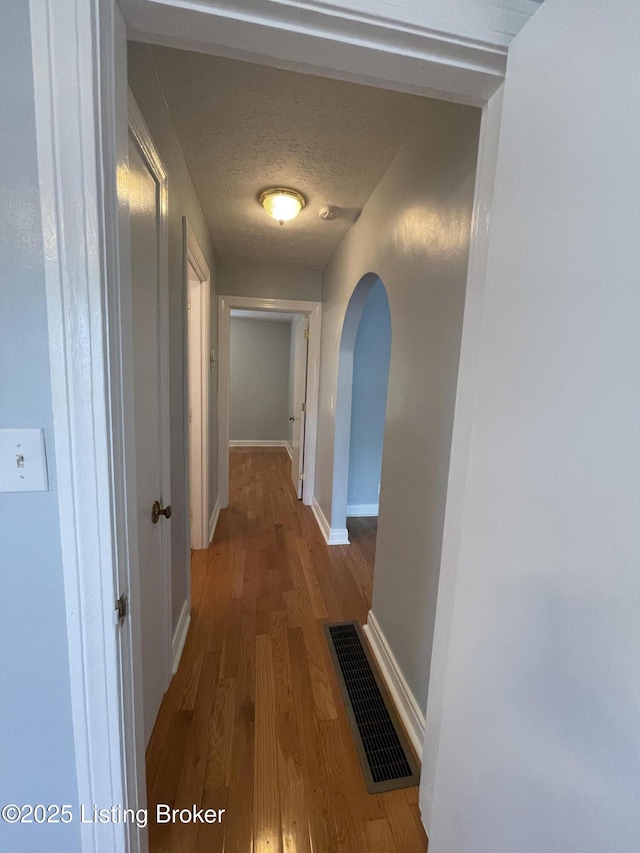 hallway with arched walkways, wood finished floors, and baseboards