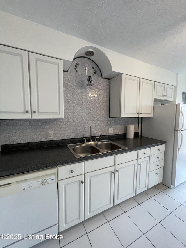 kitchen featuring white appliances, a sink, dark countertops, light tile patterned floors, and white cabinetry