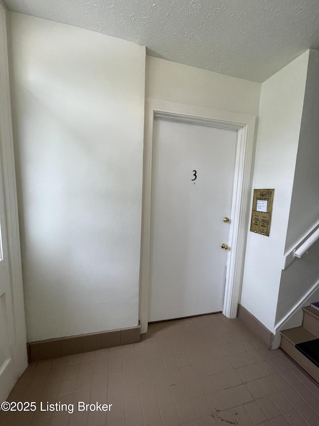 foyer featuring stairway, baseboards, and a textured ceiling