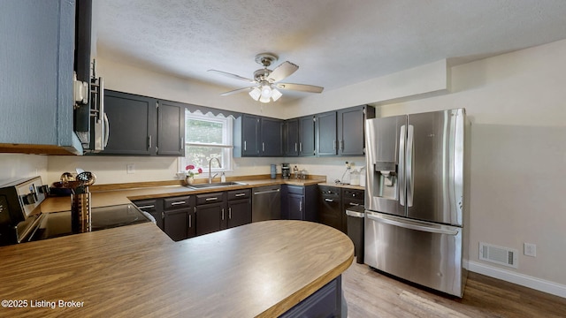 kitchen featuring stainless steel appliances, a sink, ceiling fan, baseboards, and light wood-style floors