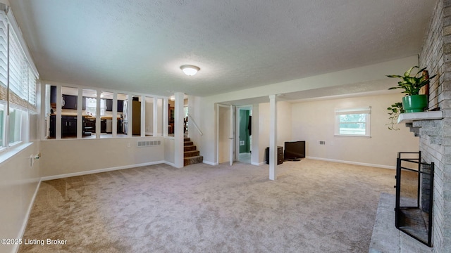 unfurnished living room with a fireplace, a textured ceiling, stairway, baseboards, and carpet flooring