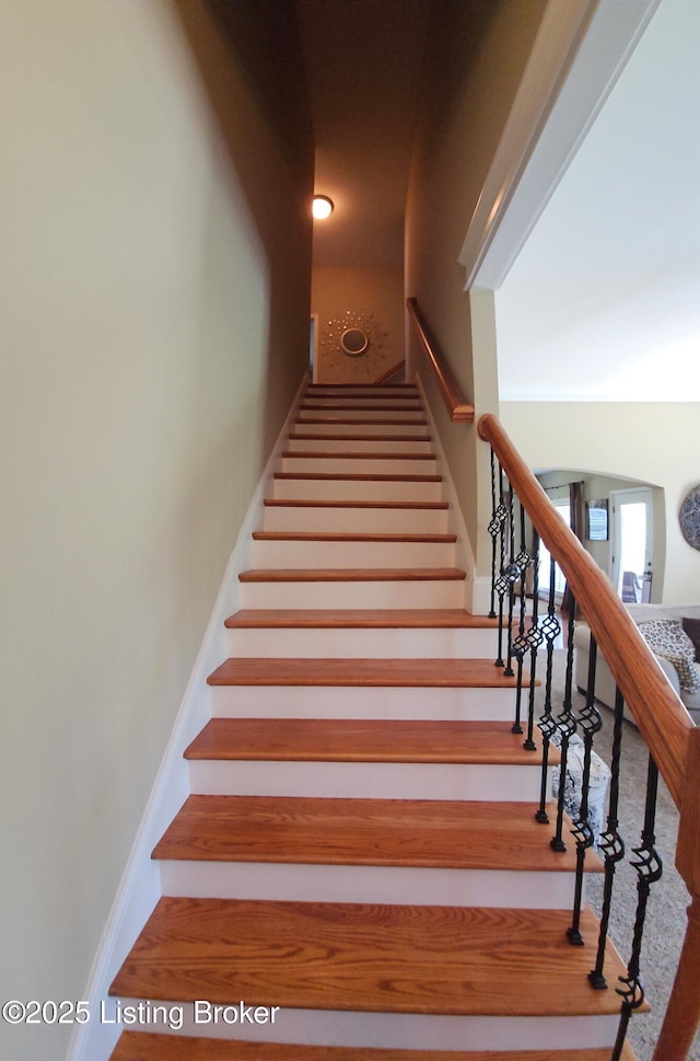 staircase featuring arched walkways and wood finished floors