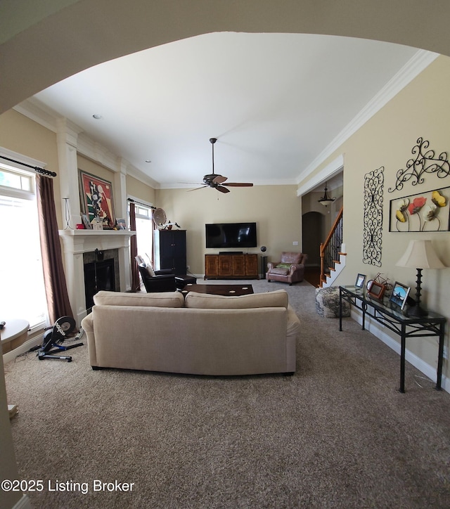 living area featuring arched walkways, crown molding, a fireplace, carpet flooring, and ceiling fan