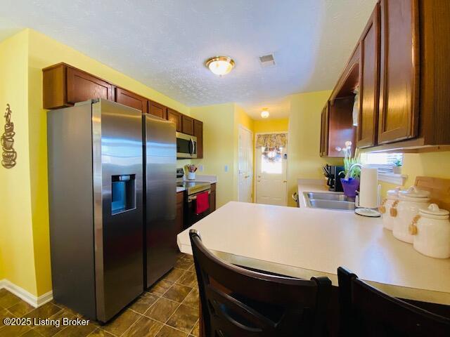 kitchen with stainless steel appliances, a sink, light countertops, a peninsula, and baseboards