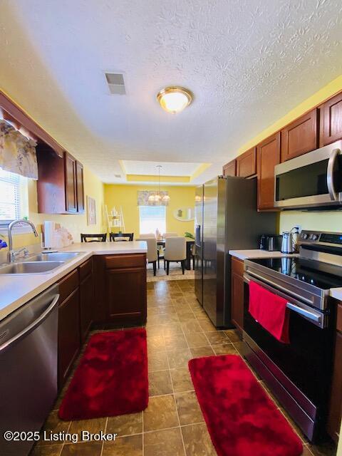 kitchen featuring appliances with stainless steel finishes, a sink, a peninsula, tile patterned flooring, and light countertops