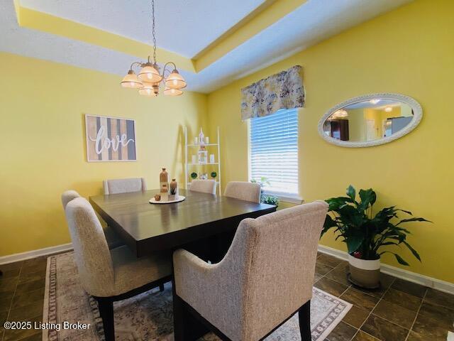dining space featuring a chandelier, baseboards, and a raised ceiling