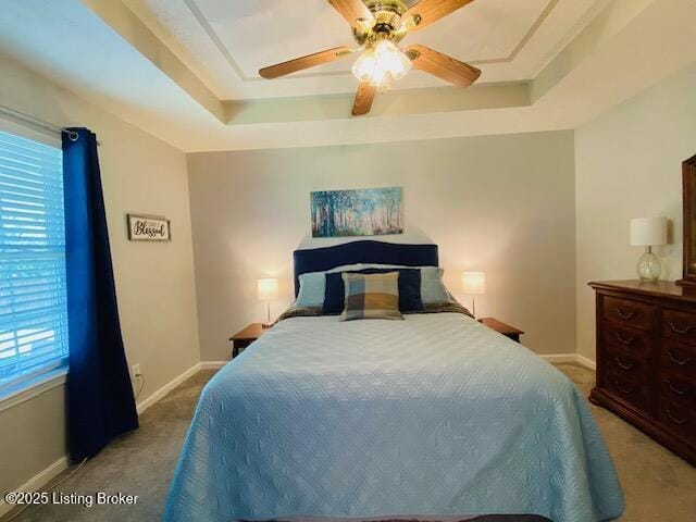 carpeted bedroom with a raised ceiling, multiple windows, and baseboards