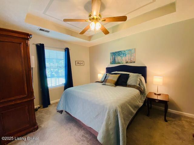 bedroom featuring a tray ceiling, light colored carpet, and baseboards